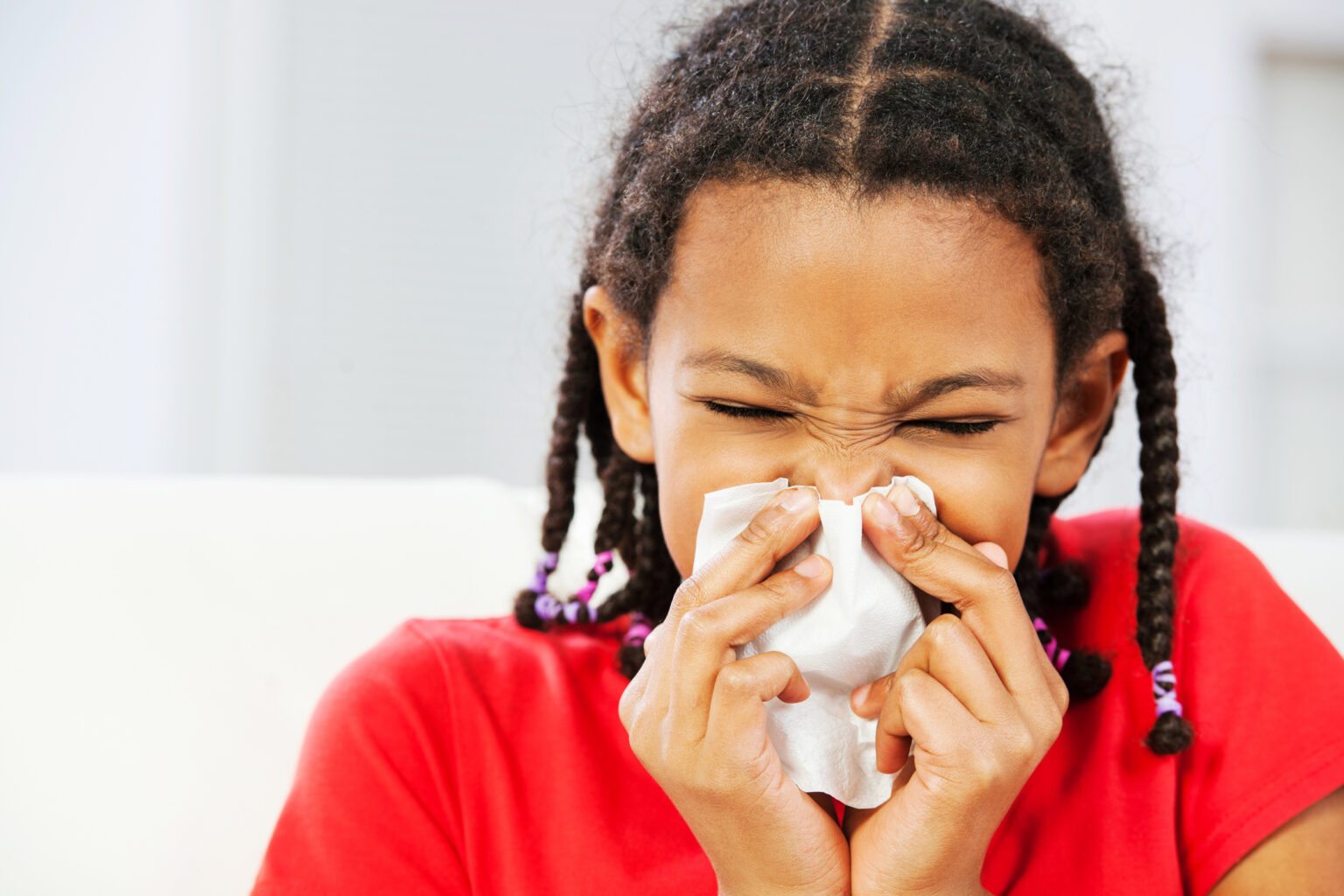 A girl is sniffing on a tissue.