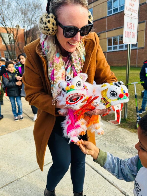 A teacher holding 2 lion puppets and a students is touching them.