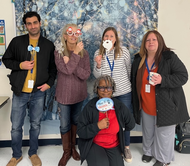 Teachers at a holiday theme photo booth (each holding different snow flakes). Ms. Harvey squad down and 3 female teachers and a male standing behind.