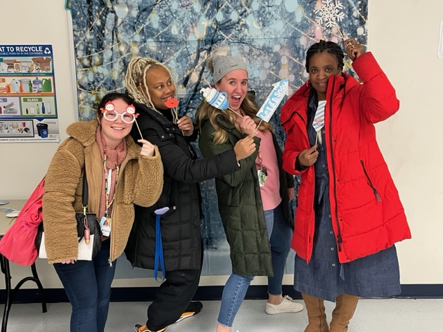 Teachers at a holiday theme photo booth (each holding different snow flakes). our female teachers posting happily for the pic.