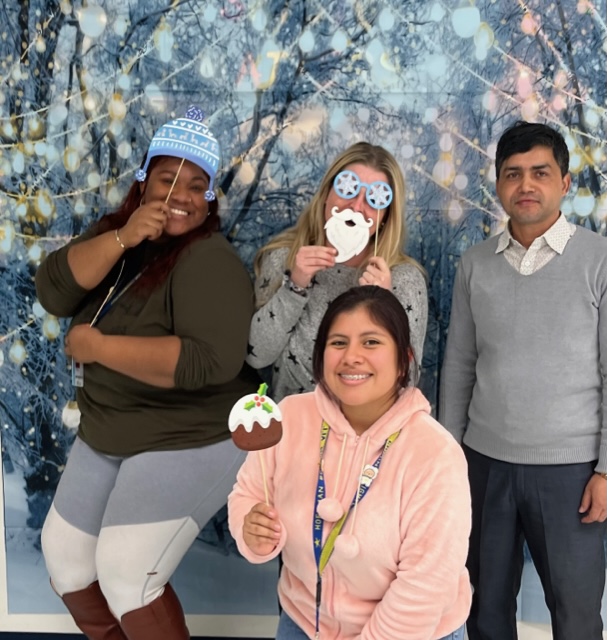 Teachers at a holiday theme photo booth (each holding different snow flakes). A male teacher on the right and two female teachers standing to the left; a female teacher squad down.