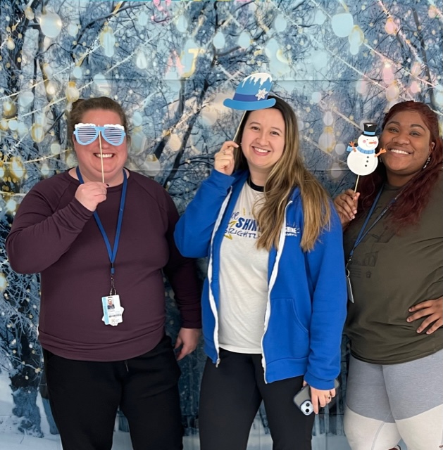 Teachers at a holiday theme photo booth (each holding different snow flakes). Ms. Liz, Ms. Goode and Ms. Aylor.