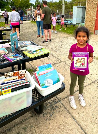 A student smiling with a book in her hand that she picked from a free books station.