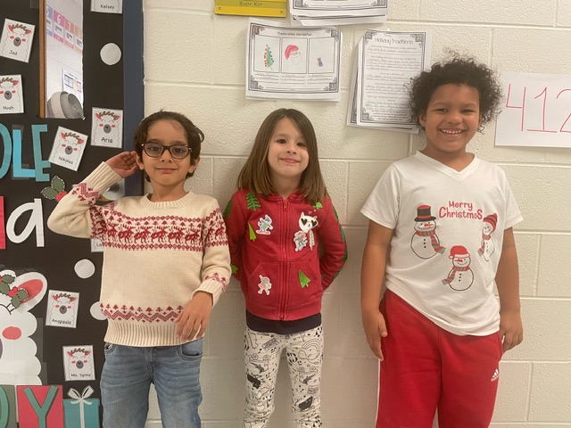 3 kindergarten students wearing holiday sweaters.