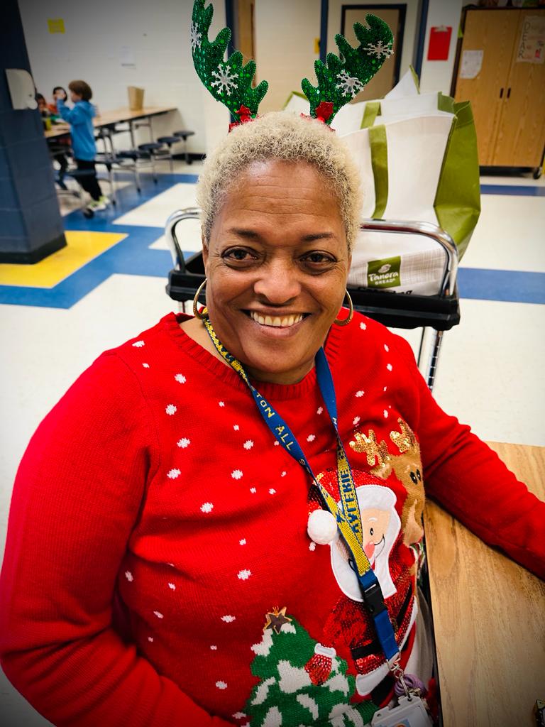 Pre-K teacher sit at a desk and she is wearing Santa sweater.