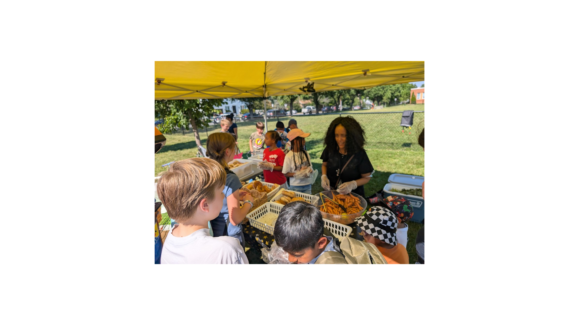 Monday share table at Hoffman-Boston; volunteers and students standing behind bagels table. A volunteer is helping a student with a selecting bagels.